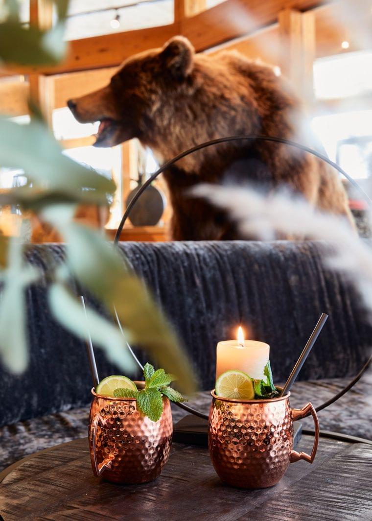 Two Moscow Mule copper mugs with mint and lime beside a candle in cozy lodge setting with bear decor